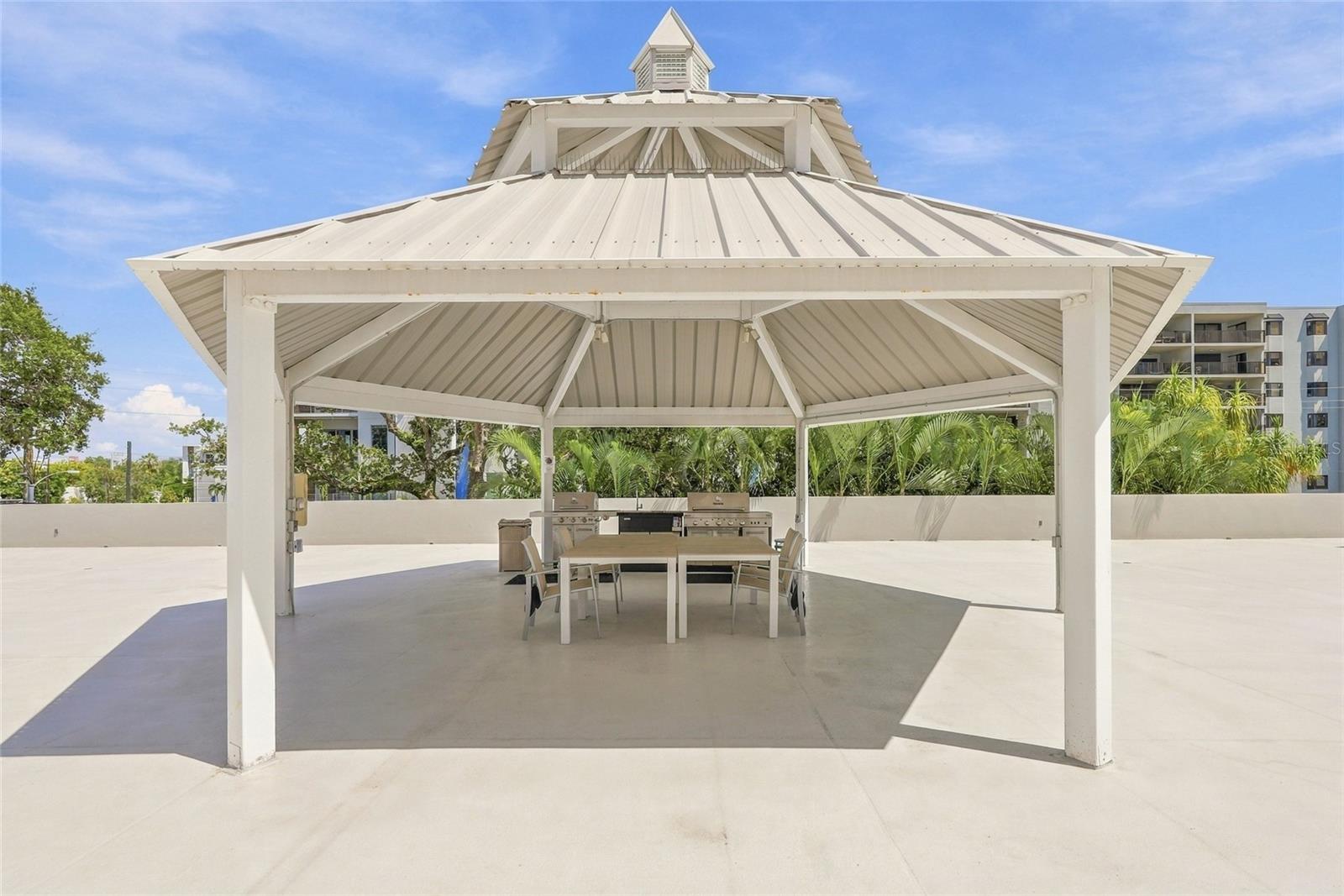 White rooftop pavilion with an outdoor dining table and built-in grills.