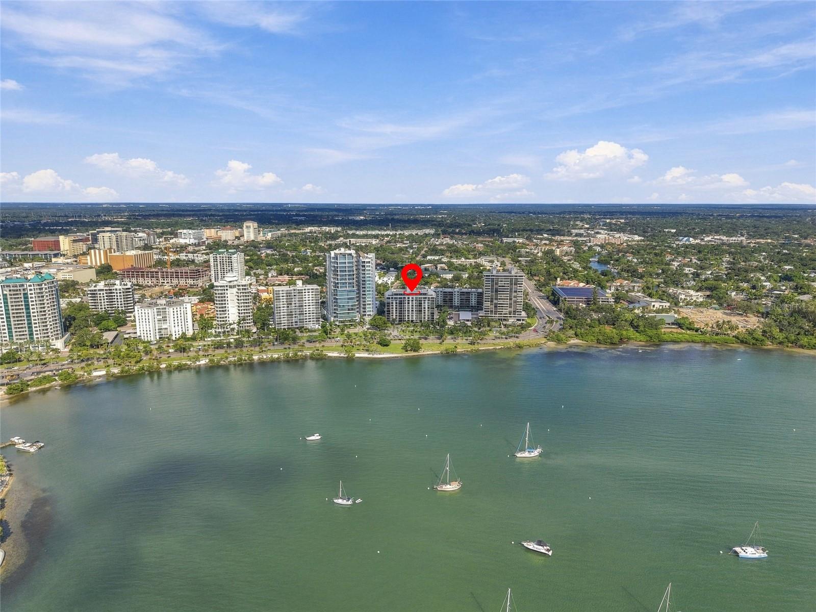 Aerial view of a waterfront condominium marked by a red pin, with sailboats on the bay.