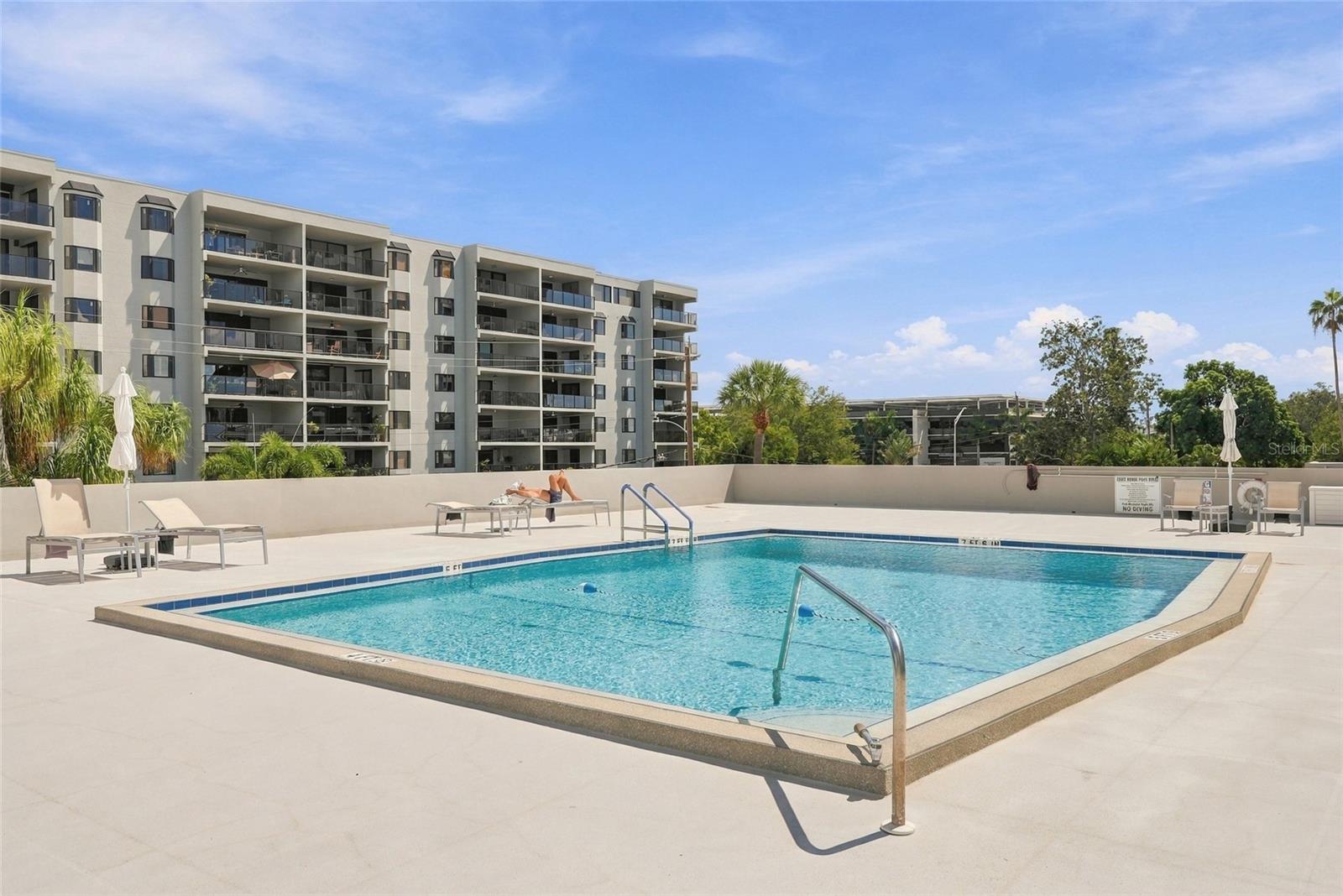 Condominium pool deck with lounge chairs and the apartment building behind it.