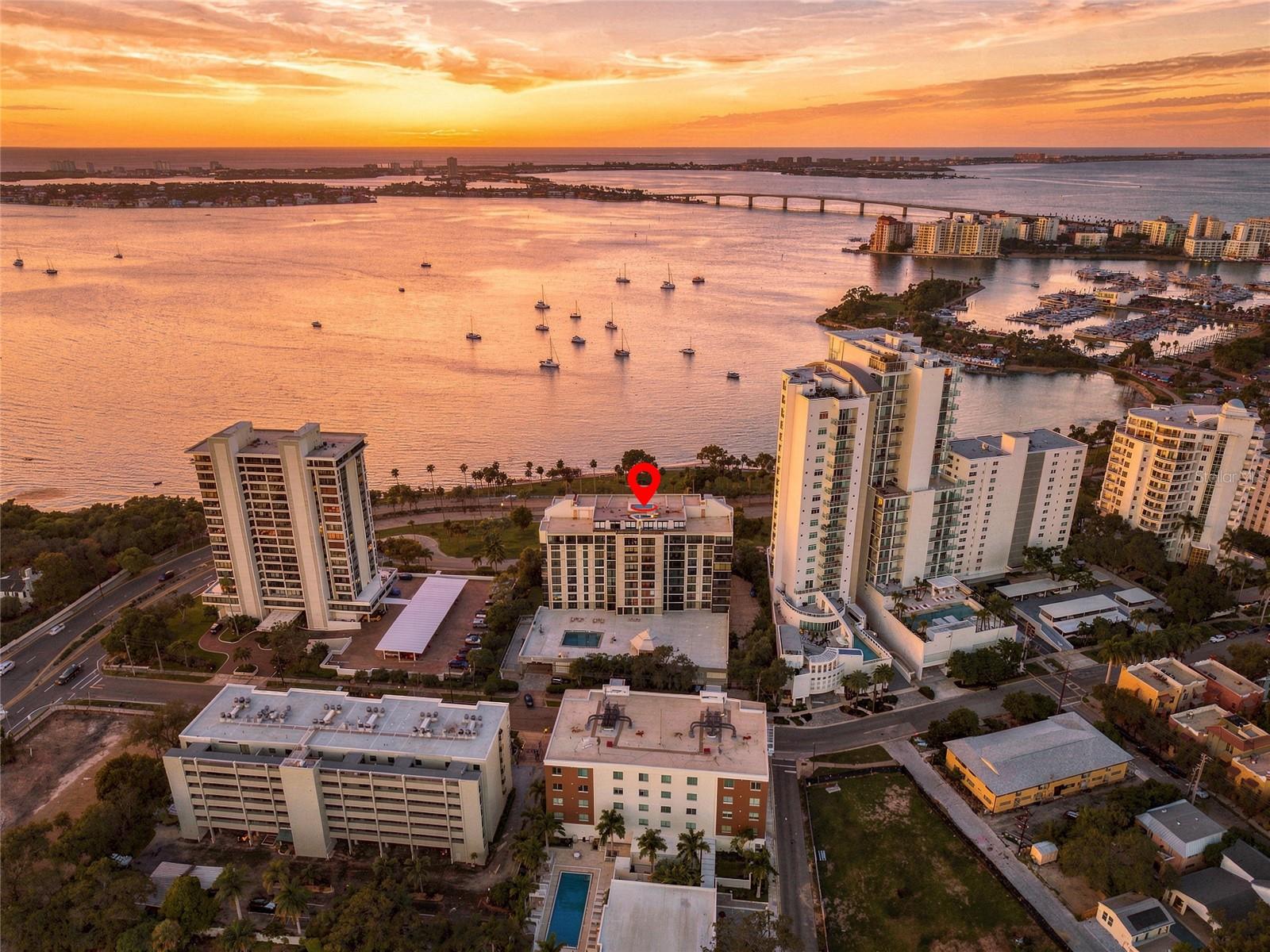 Waterfront condominium buildings beside Sarasota Bay at sunset, with a red marker identifying one building.