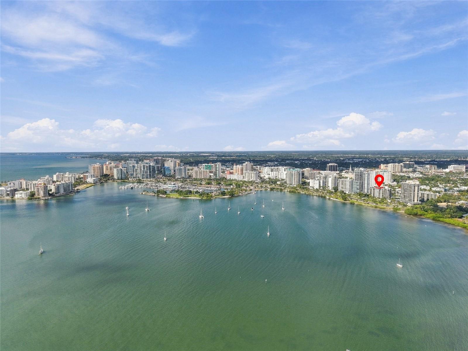 Aerial view of Sarasota waterfront and bay, with a red pin marking the property among the shoreline towers.