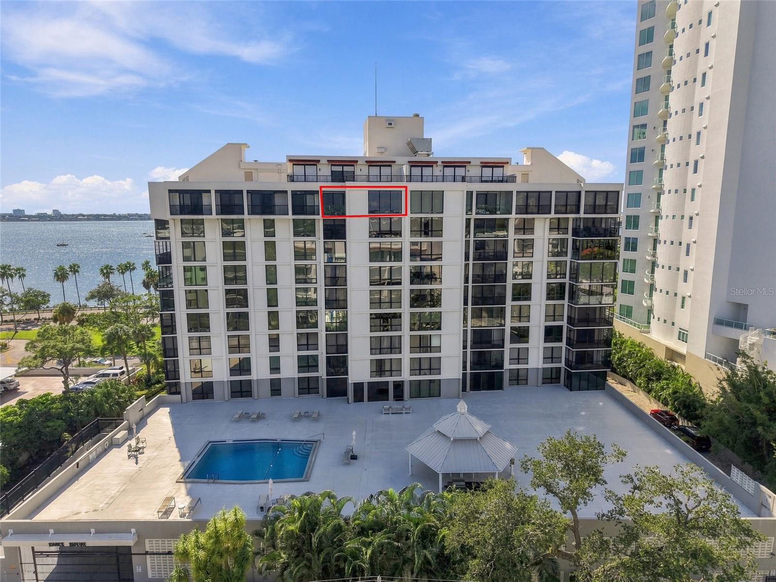 Condominium building beside the water, with the featured unit outlined in red and a pool below.