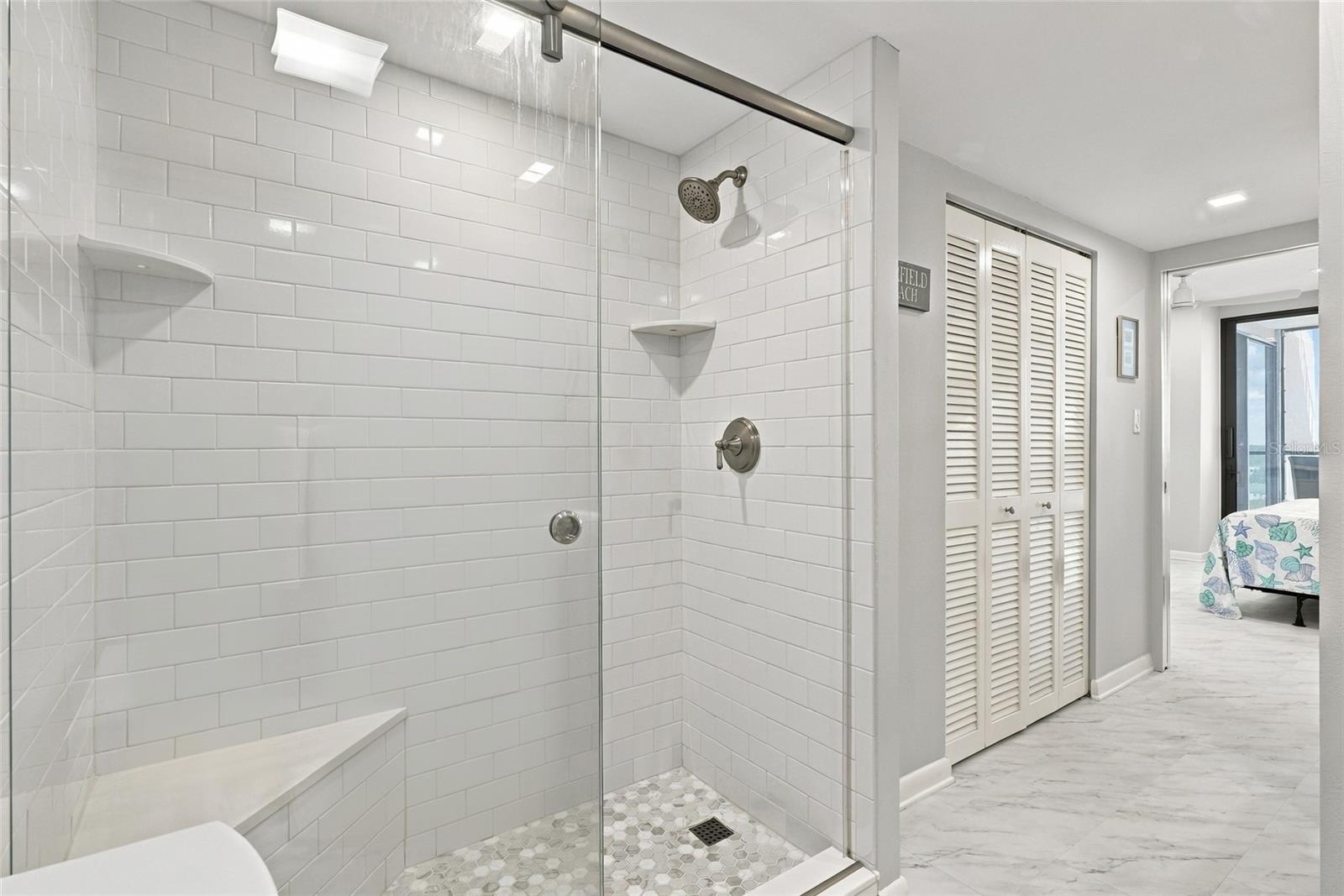 Bathroom with a glass-enclosed shower, white subway tile, corner shelves, and a hexagonal mosaic floor.