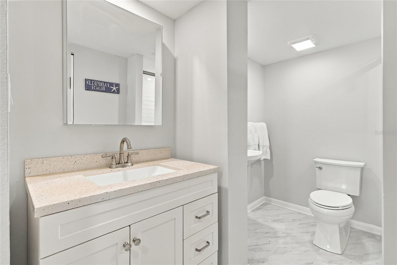 Bathroom with a white vanity, speckled countertop, and marble-look floor.