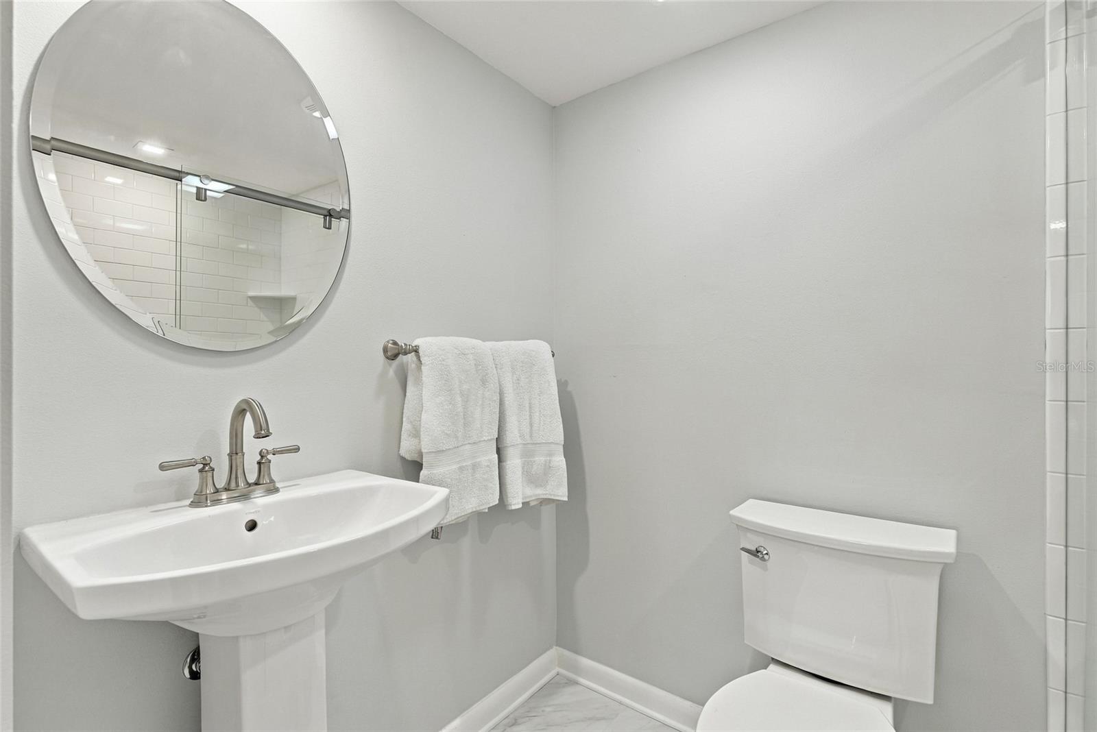 Bathroom with a pedestal sink, round mirror, white towels, and subway-tile shower reflected in the mirror.