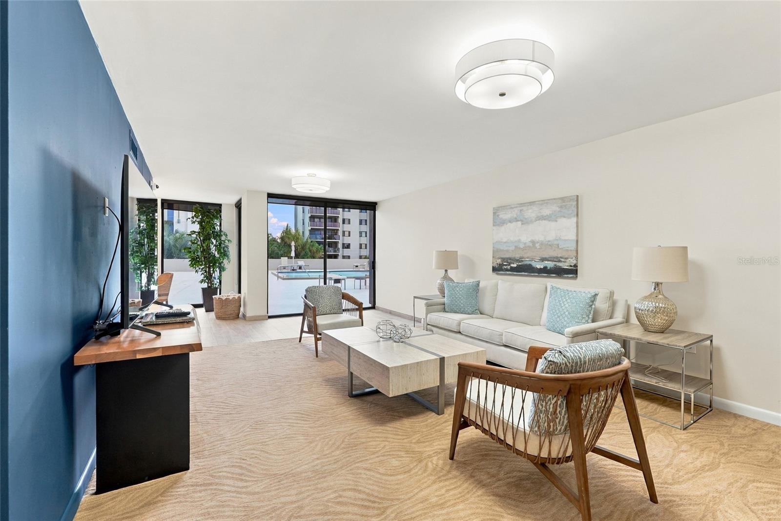 Staged living room with a blue accent wall, cream sofa, and windows overlooking a courtyard pool.