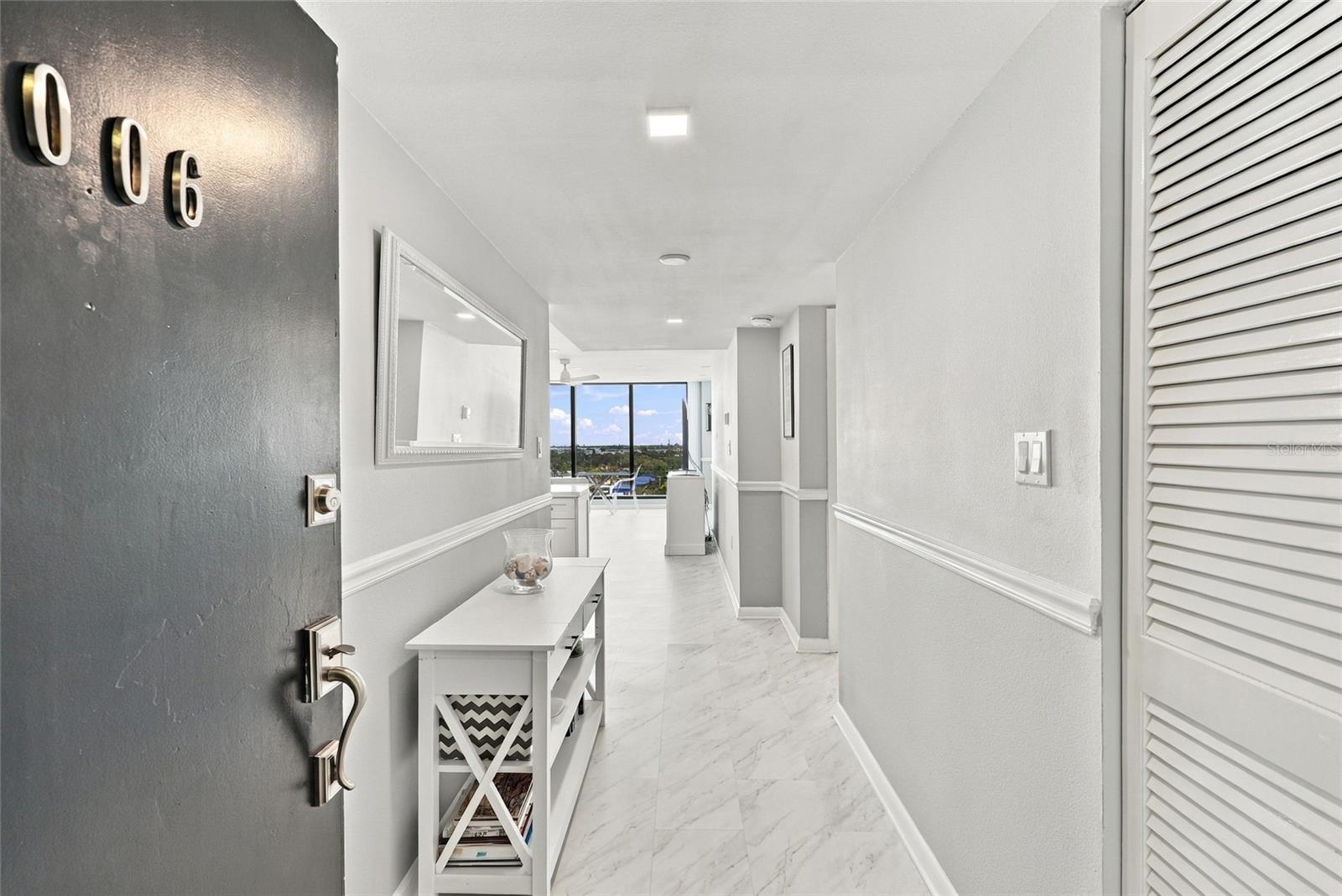 Condominium entry hallway with marble-look flooring, a console table, and distant views through end windows.