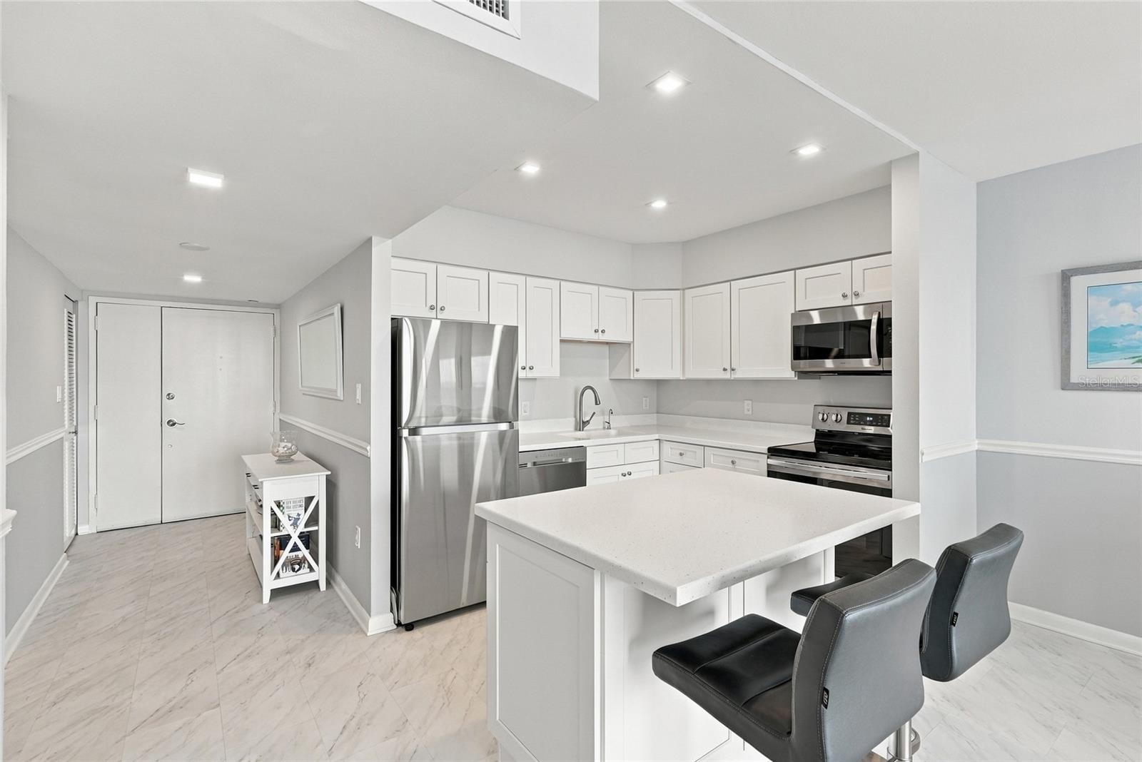 Modern condo kitchen with white cabinetry, stainless steel appliances, and a large island with bar seating.