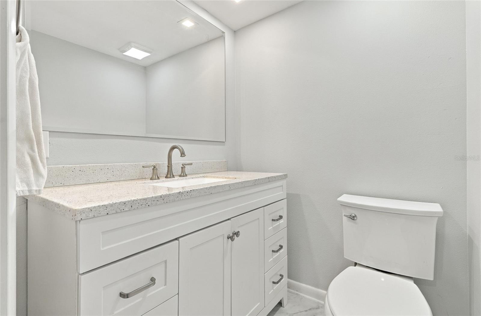 Bathroom vanity with a speckled countertop and large mirror beside a white toilet.