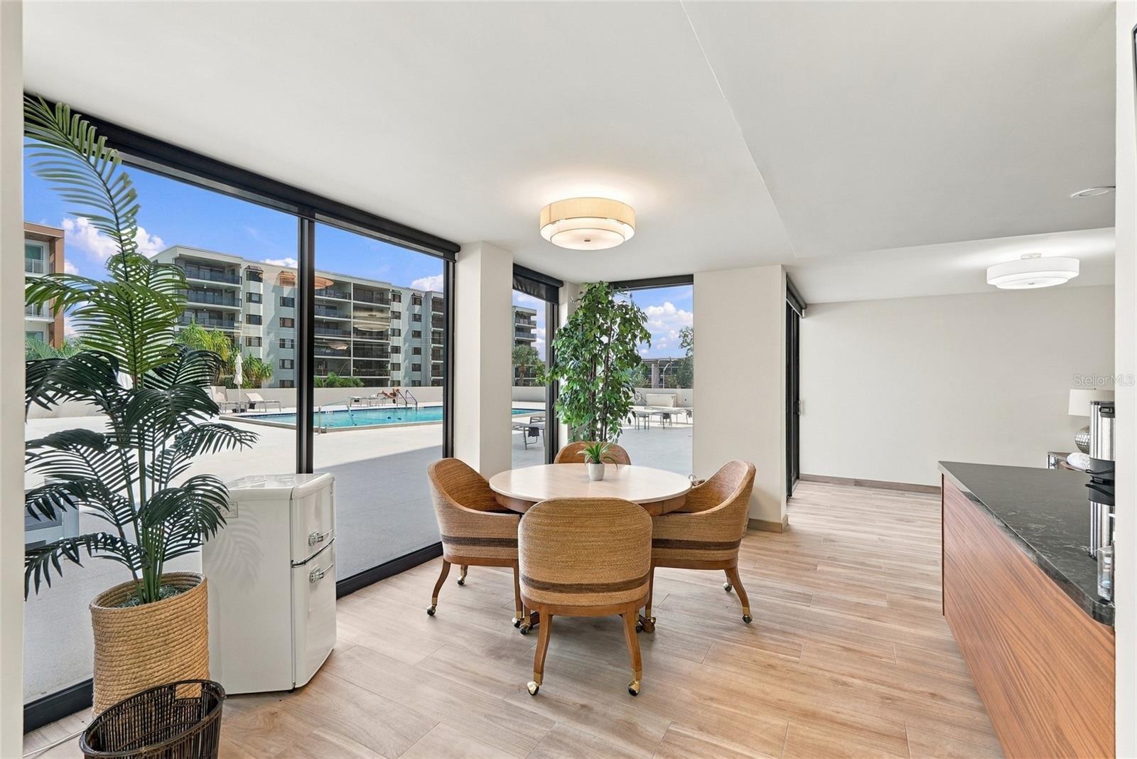 Condo dining area with floor-to-ceiling windows overlooking a swimming pool.