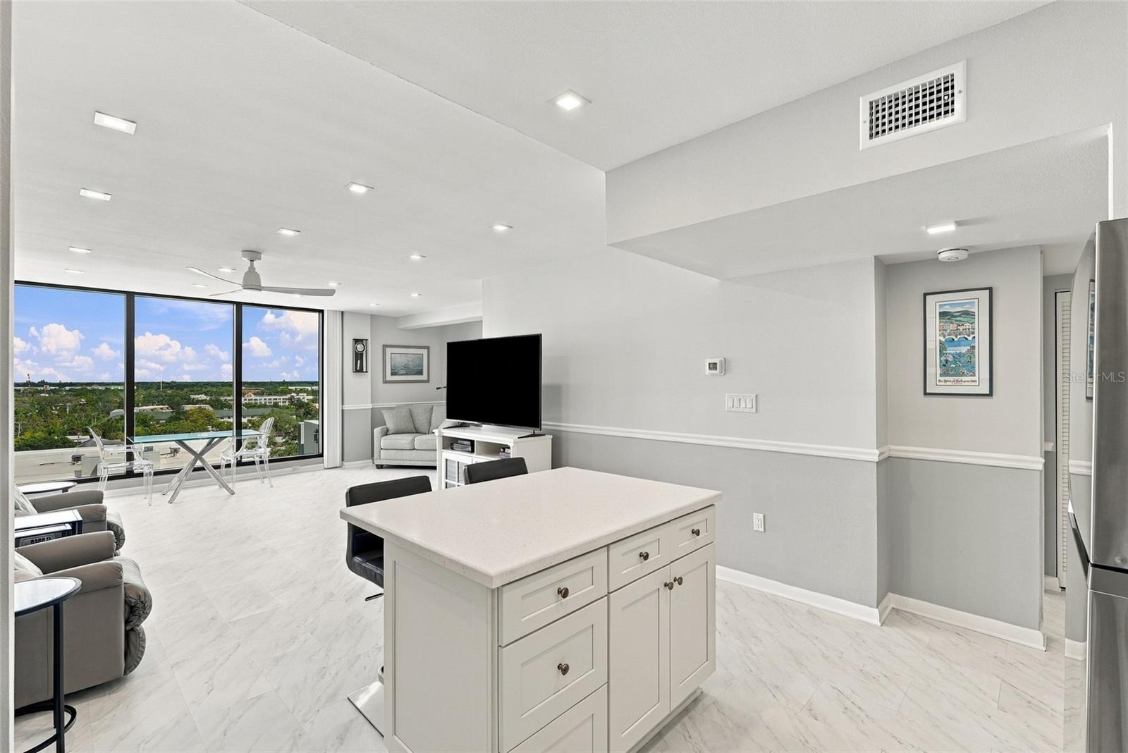 Open condo kitchen and living area with a large island and floor-to-ceiling windows overlooking the city.