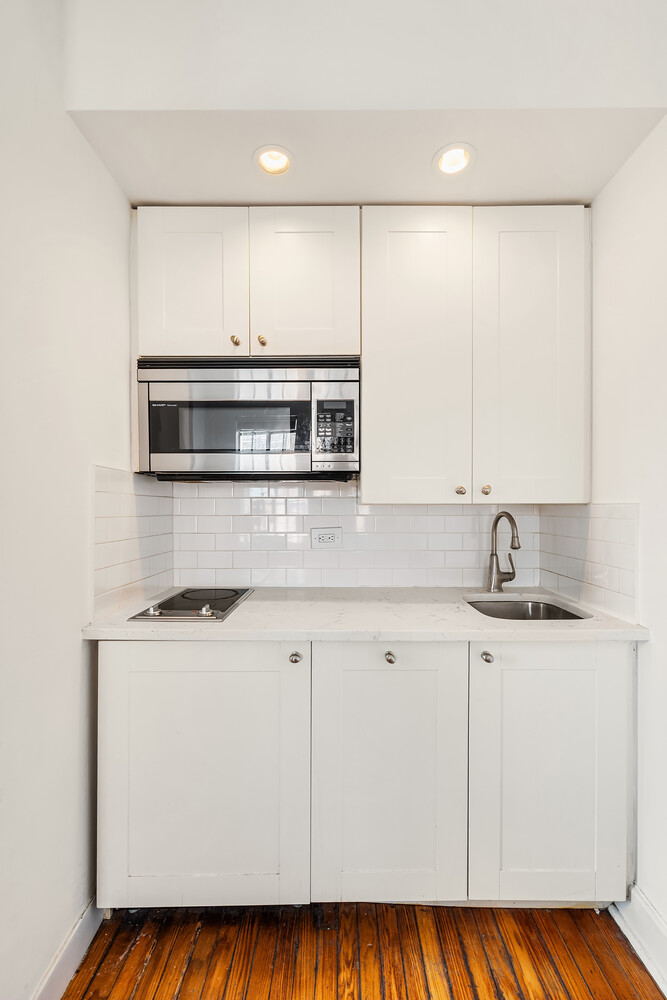 Compact white kitchen with a built-in microwave, cooktop, subway-tile backsplash, and polished wood floor.