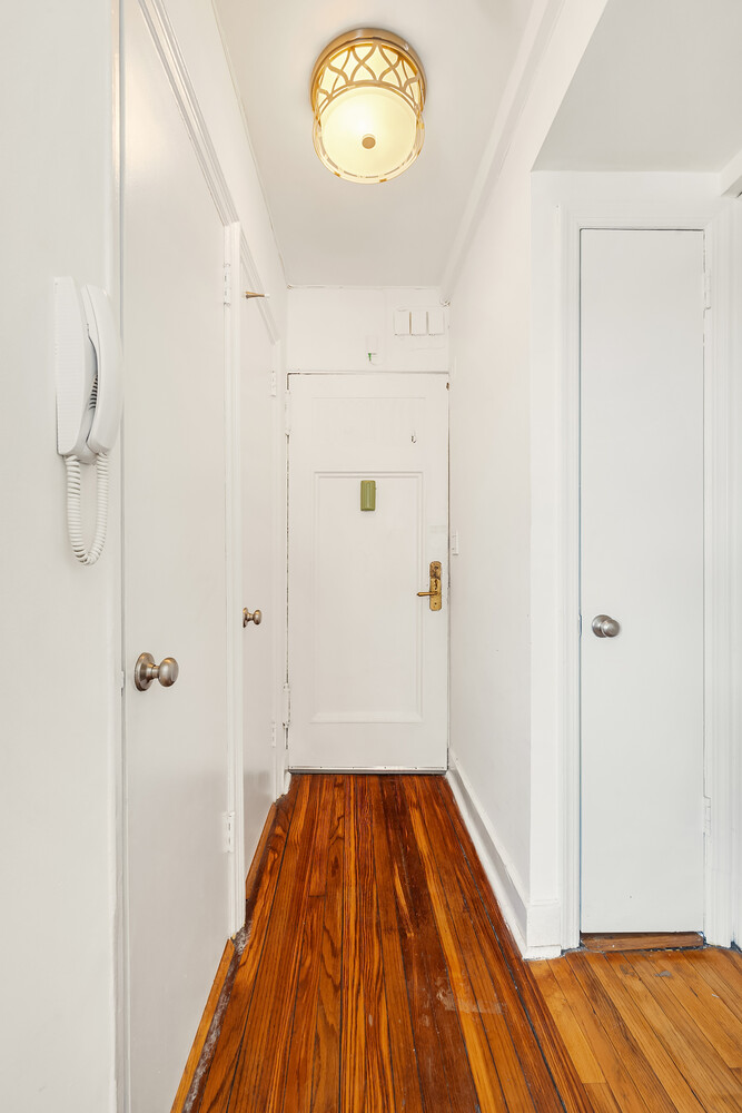 Apartment entry hallway with polished hardwood floors, a white front door, and wall intercom.
