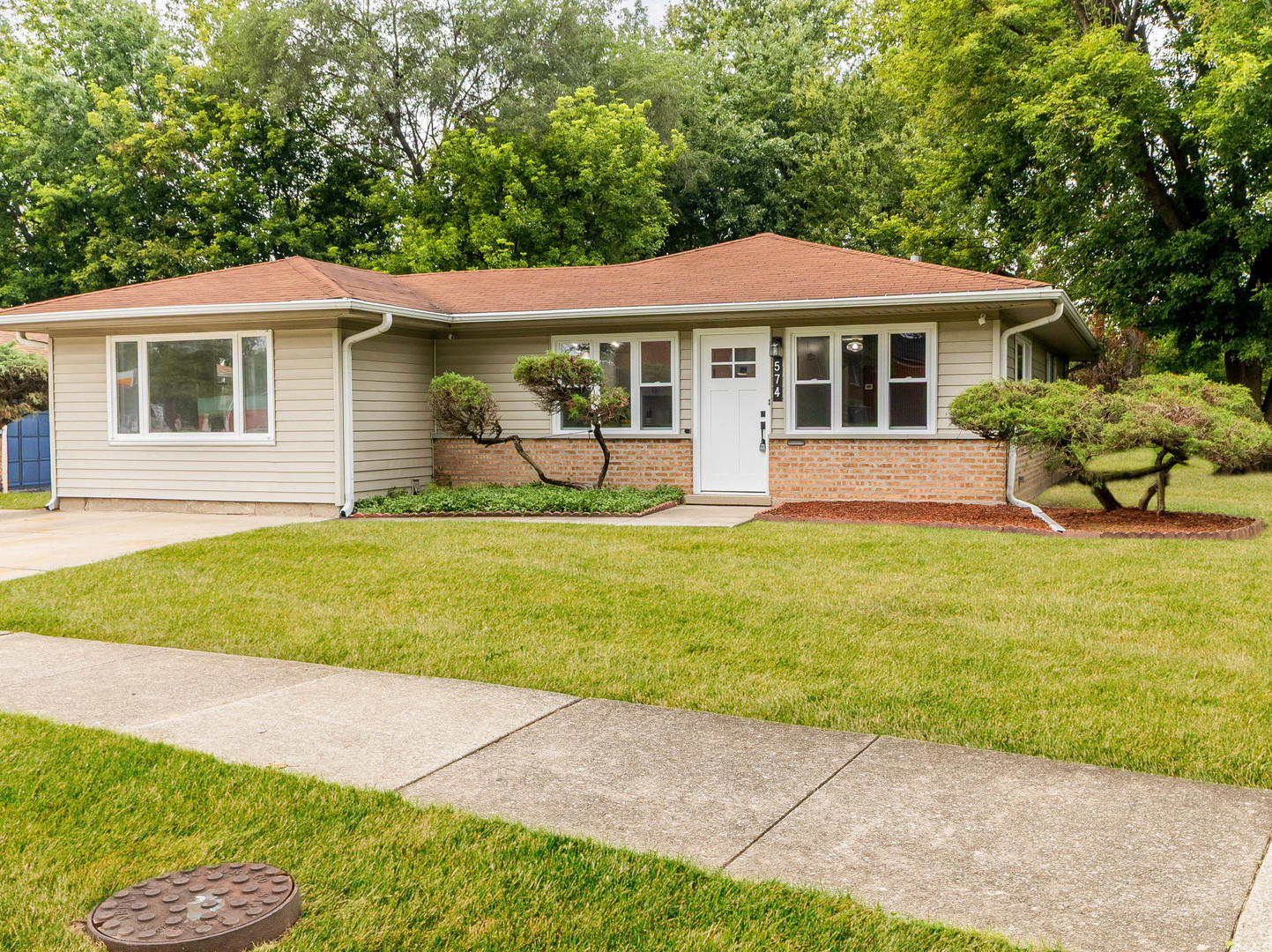 Single-story ranch house with beige siding, brick accents, and landscaped front lawn.
