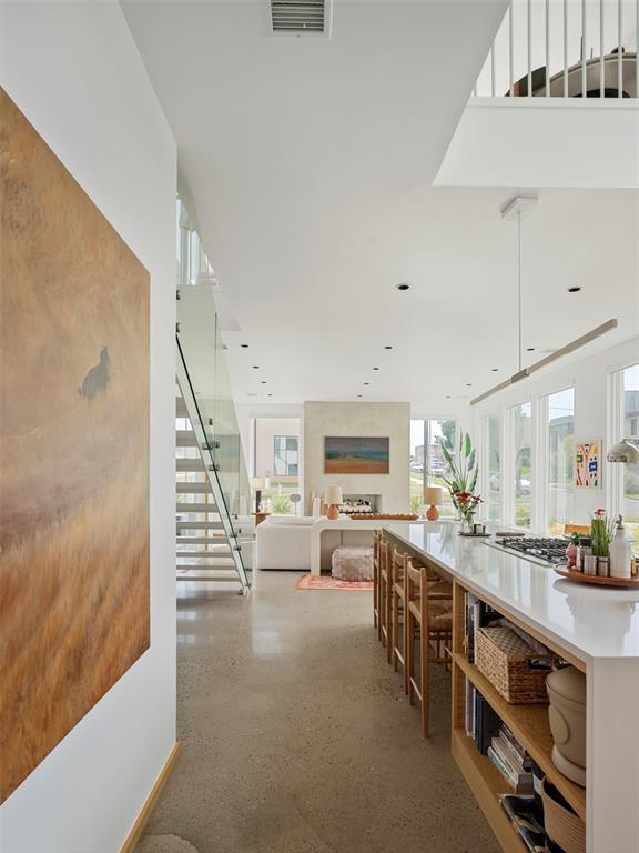 Modern kitchen with a long white island, wooden bar stools, open shelving, and a staircase.