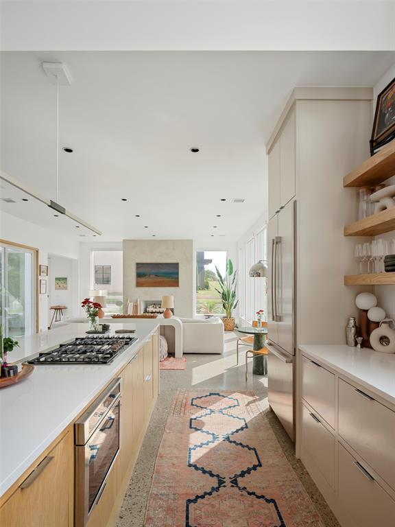 Bright kitchen with pale wood cabinets, a large gas cooktop, and a patterned runner leading to the living area.