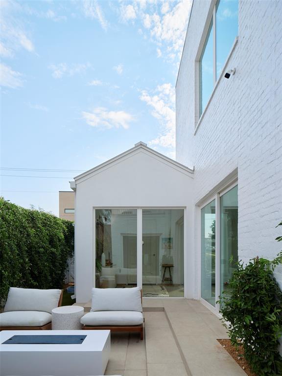 Tiled patio with cushioned lounge chairs and a fire table beside white brick walls and sliding glass doors.