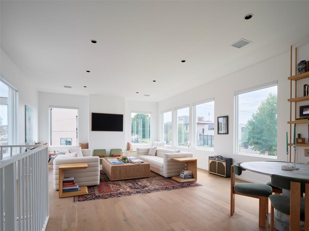 Staged living room with a large sectional, patterned rug, pale wood floors, and expansive windows.