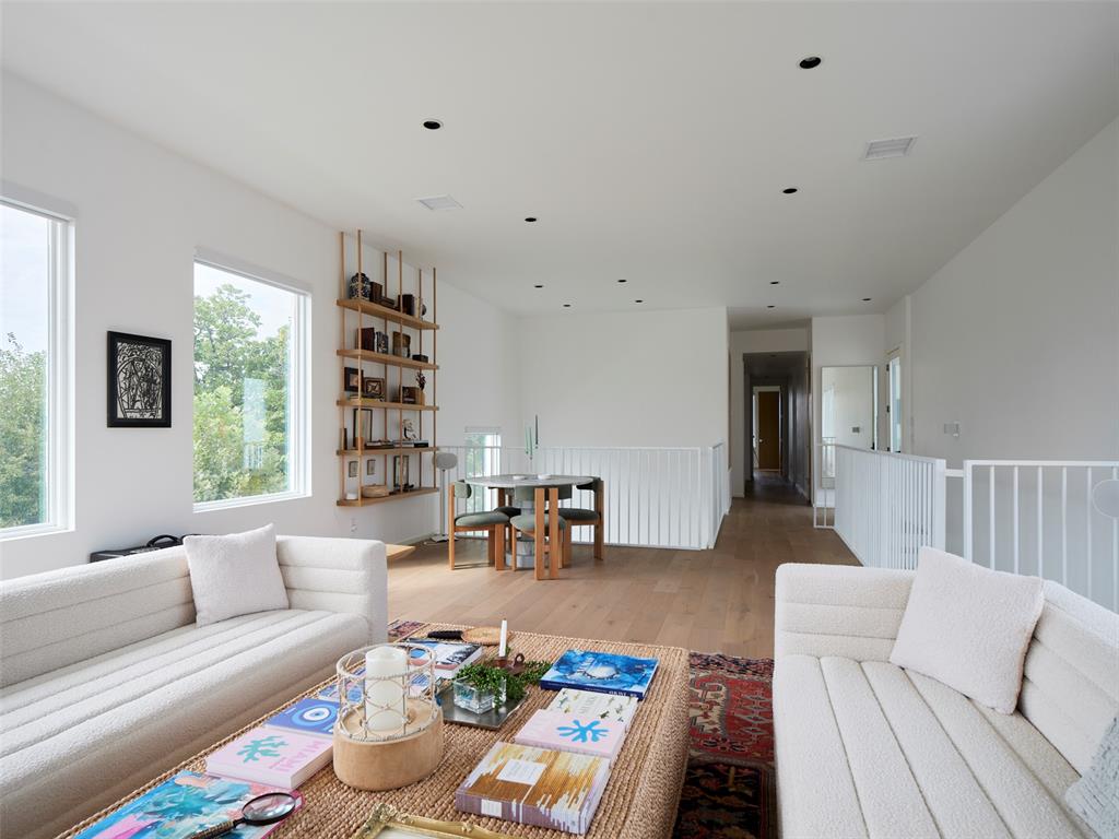 Open living room with white sofas, a woven coffee table, large windows, and a dining nook.