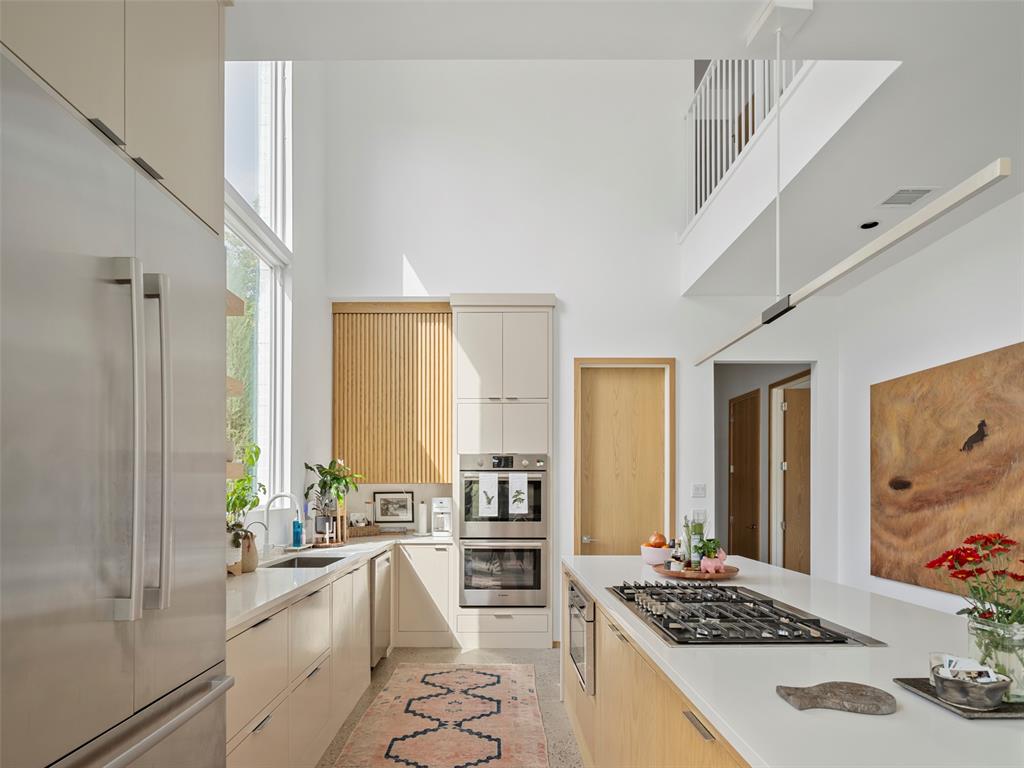 Bright modern kitchen with a gas cooktop island, light wood cabinetry, and a double-height ceiling.
