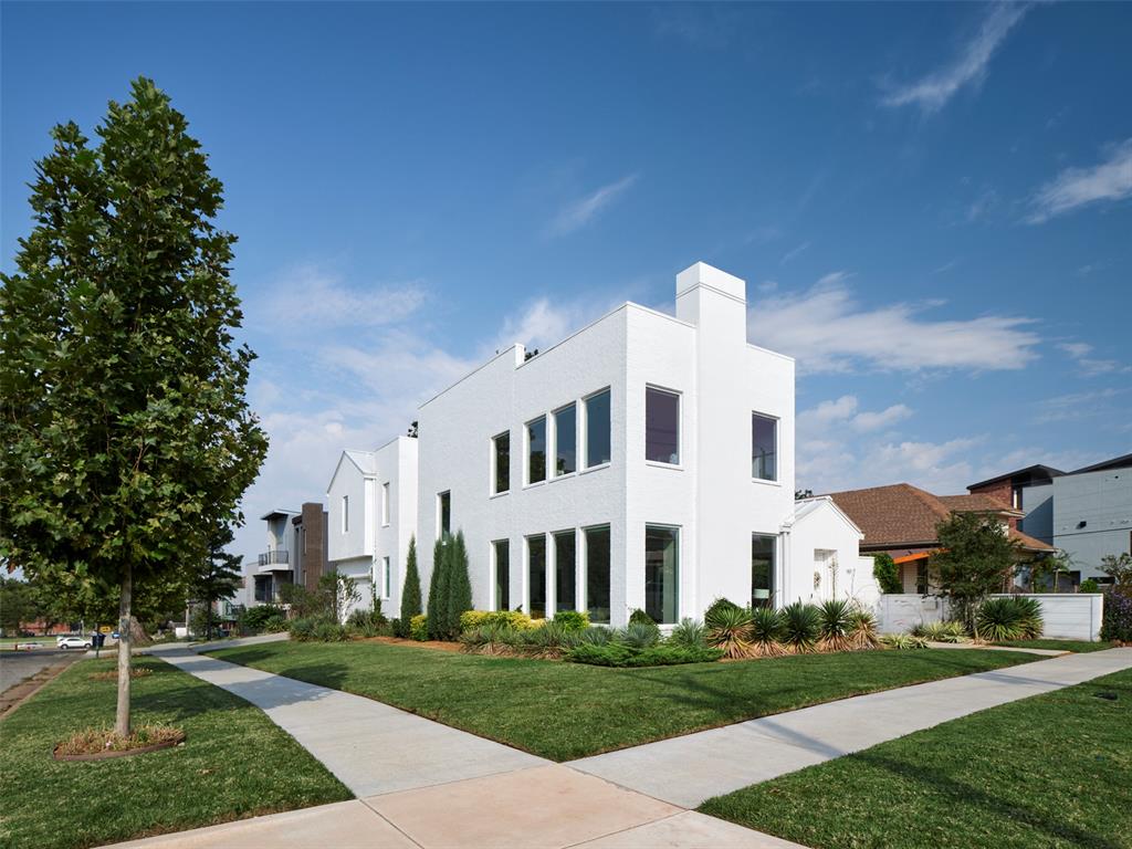 Modern white two-story house with large windows and landscaped corner lawn.