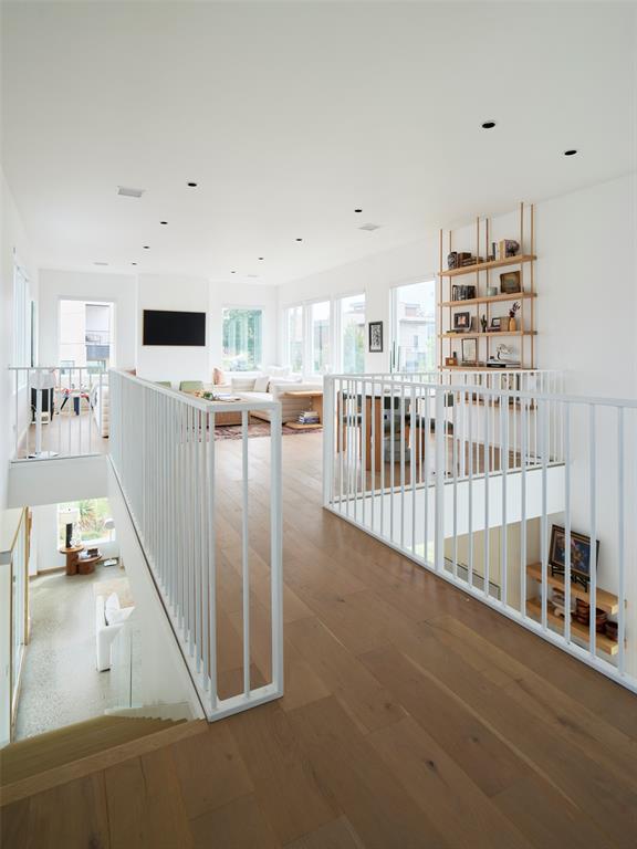 Open landing overlooking a bright living room, with white railings, wood floors, and a built-in bookshelf.