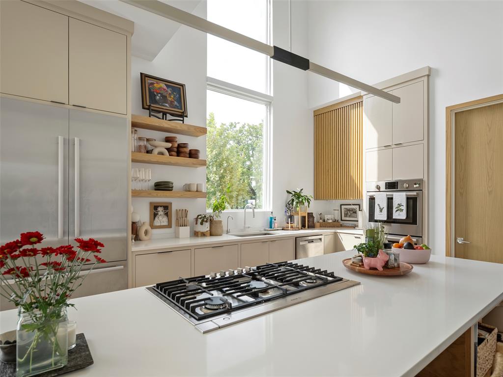 Modern kitchen with a white island and gas cooktop, tall window, and open wood shelving.