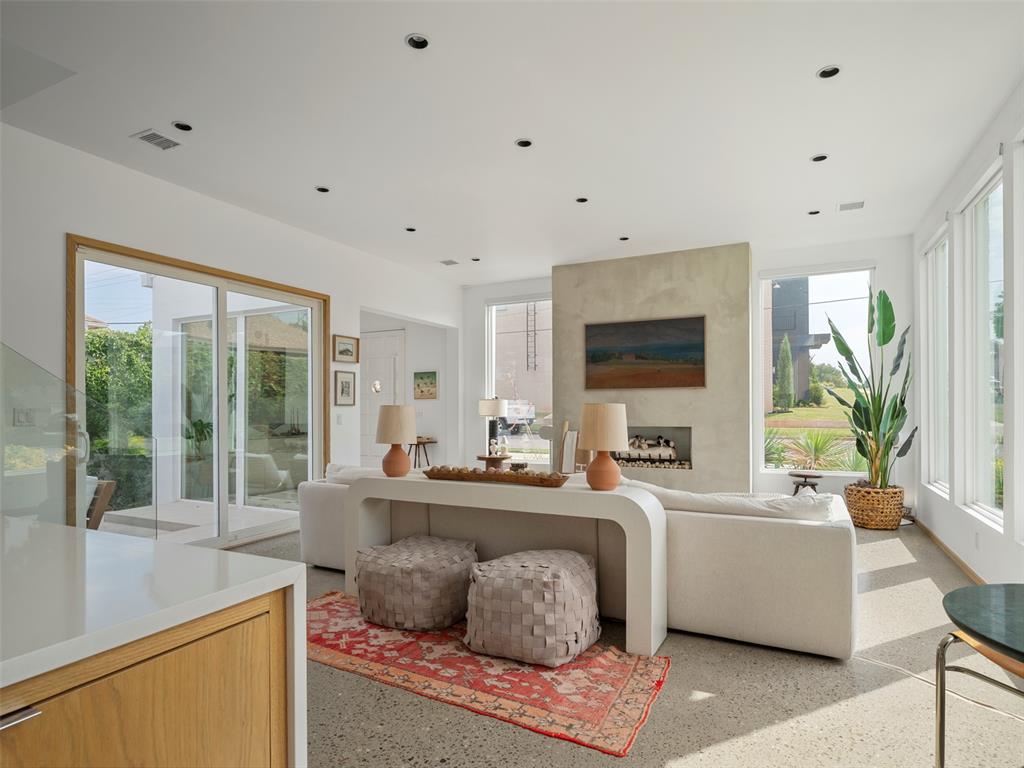 Bright living room with a modern fireplace, white sectional, large windows, and red patterned rug.