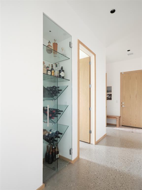 Hallway with a glass wine display, terrazzo floor, and light wood doors.
