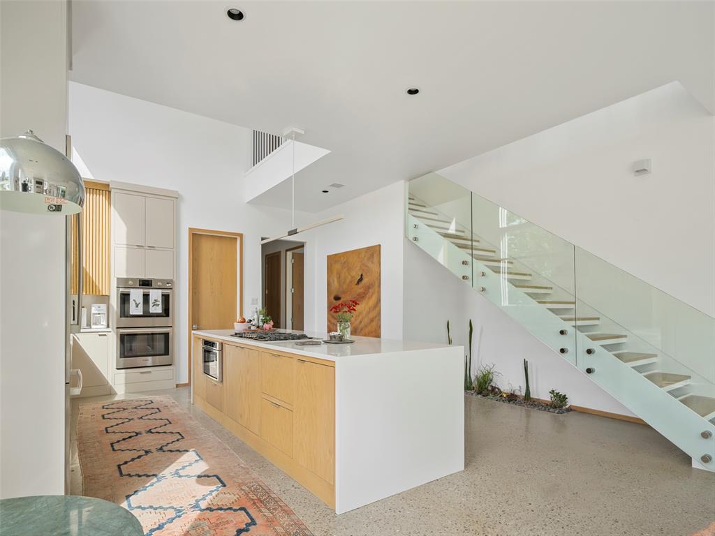 Modern kitchen with a light wood island beside a glass-railed staircase.