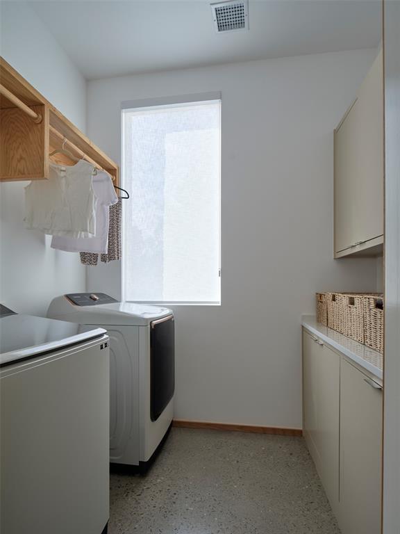 Laundry room with washer and dryer, white cabinetry, a wooden hanging rail, and a shaded window.