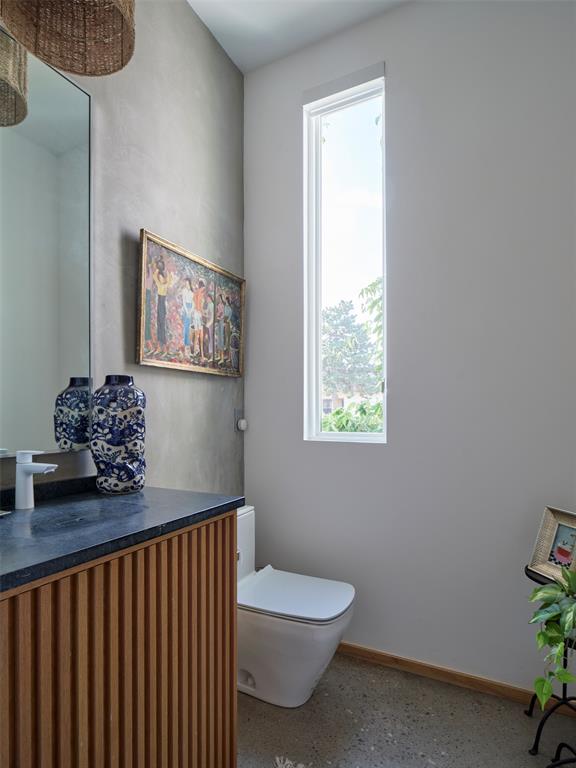 Modern bathroom with a wood-slat vanity, dark countertop, white toilet, and tall narrow window.