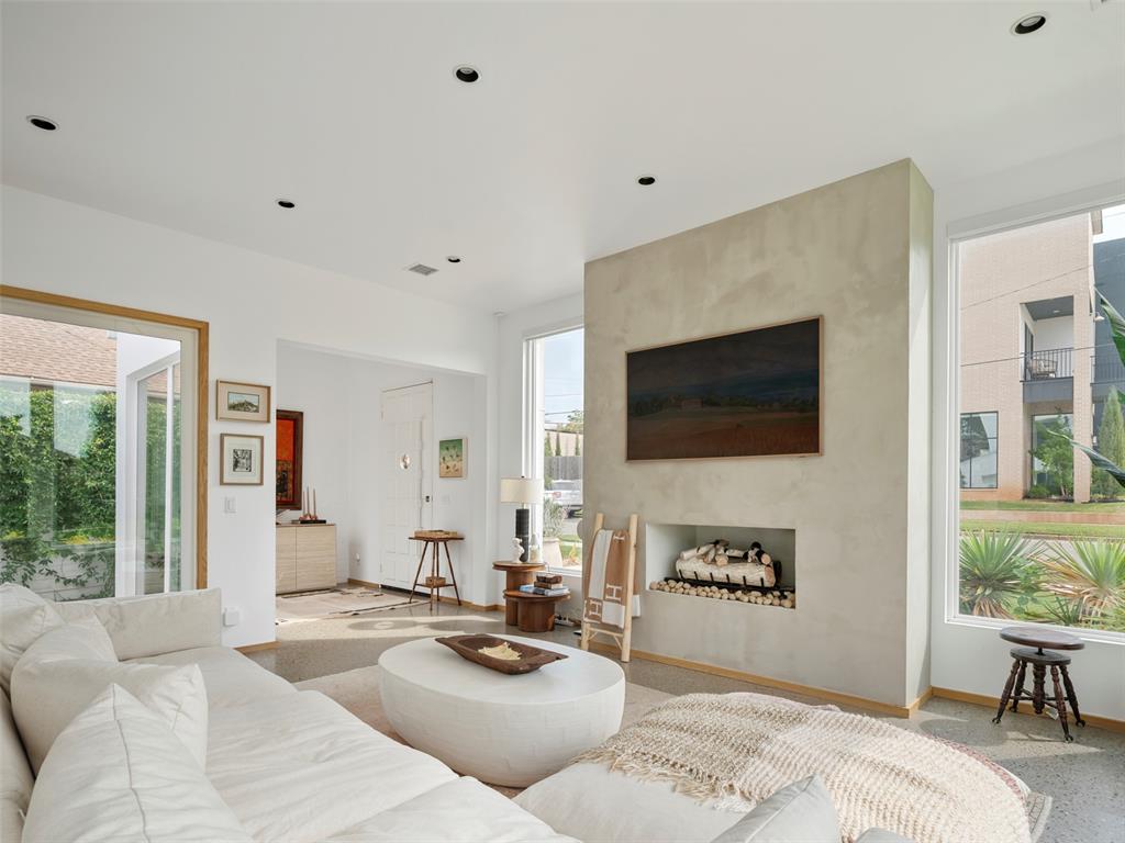 Living room with a white sectional, minimalist fireplace, and large windows overlooking greenery.