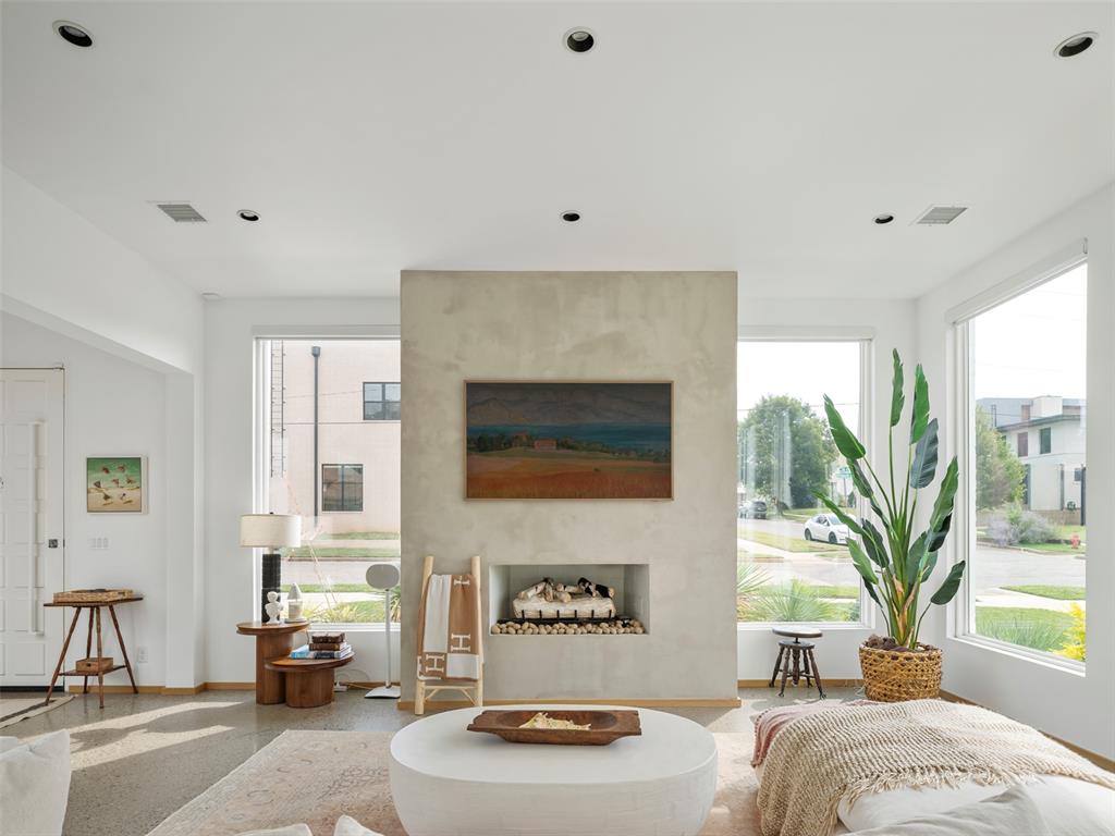 Staged living room with a plaster fireplace, tall windows, and polished concrete floors.