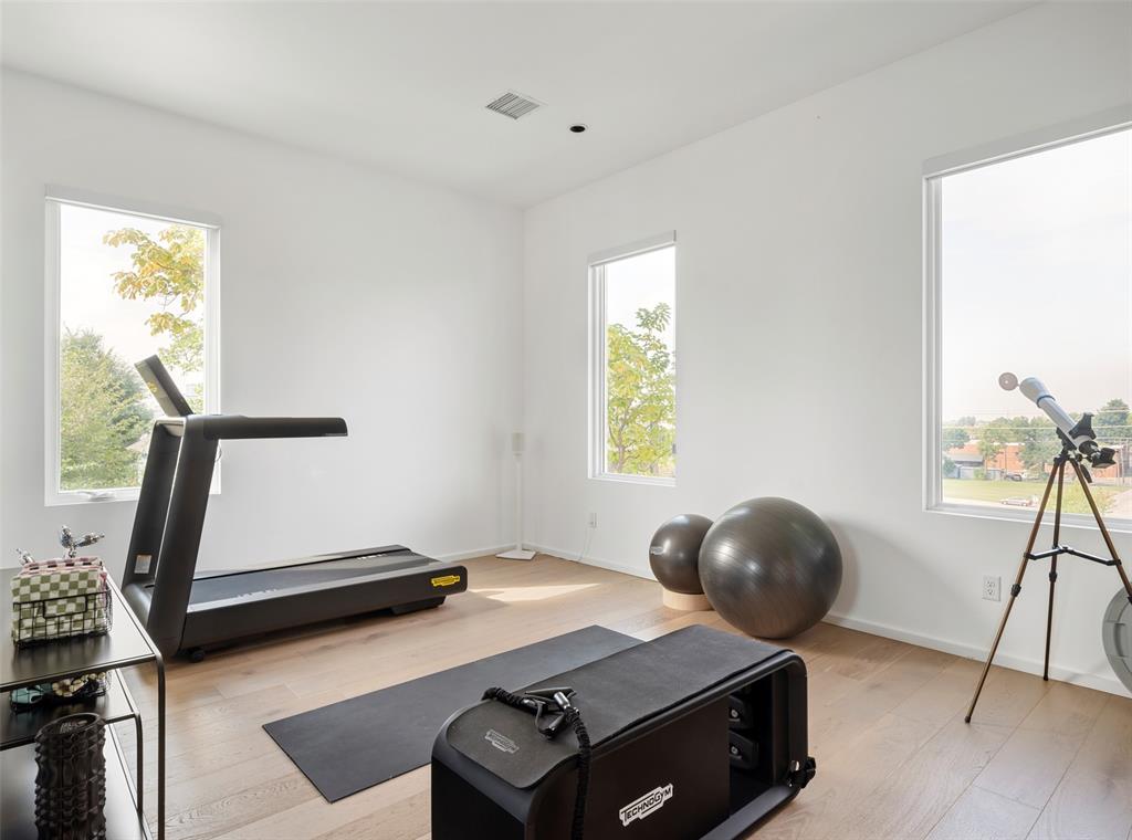 Exercise room with a treadmill, Pilates reformer, exercise balls, and a telescope beside large windows.