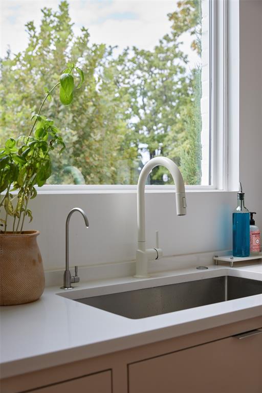 Kitchen sink beneath a wide window, with a tall white faucet and potted plant.
