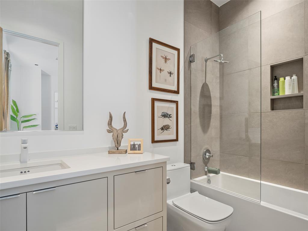 Modern bathroom with a white vanity and glass-enclosed tub-shower against beige tile.