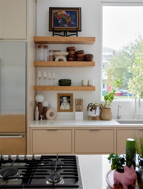 Kitchen with beige cabinets, open wooden shelves, and a sink beside a large window.