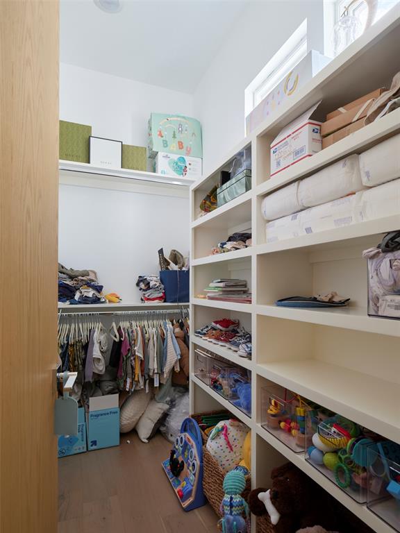 Walk-in closet with white shelving, children’s clothes, toys, and a high window.