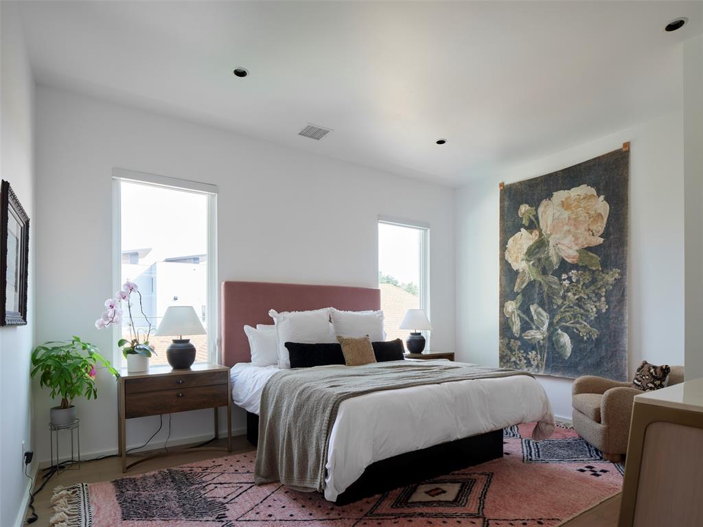 Bedroom with a rose headboard, white bedding, tall windows, and a large floral wall hanging.