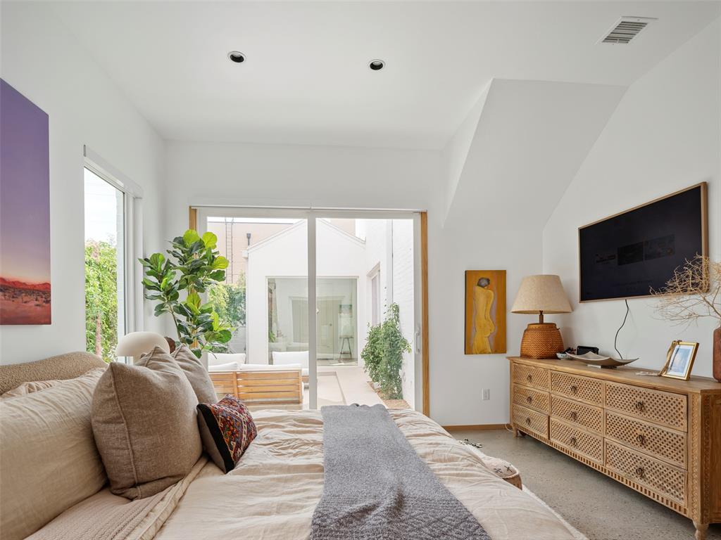 Bedroom with neutral bedding and sliding glass doors opening to a courtyard patio.