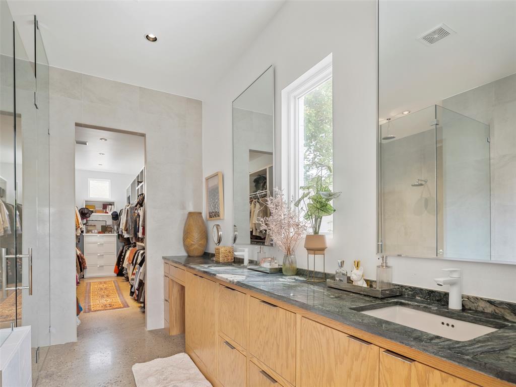 Bathroom with a long wood vanity, dark stone countertop, and glass-enclosed shower beside a walk-in closet.