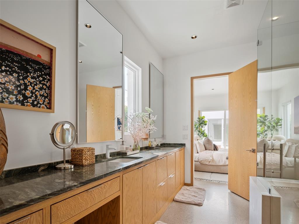 Bathroom with a long stone vanity, light wood cabinetry, large mirrors, and a glass shower.