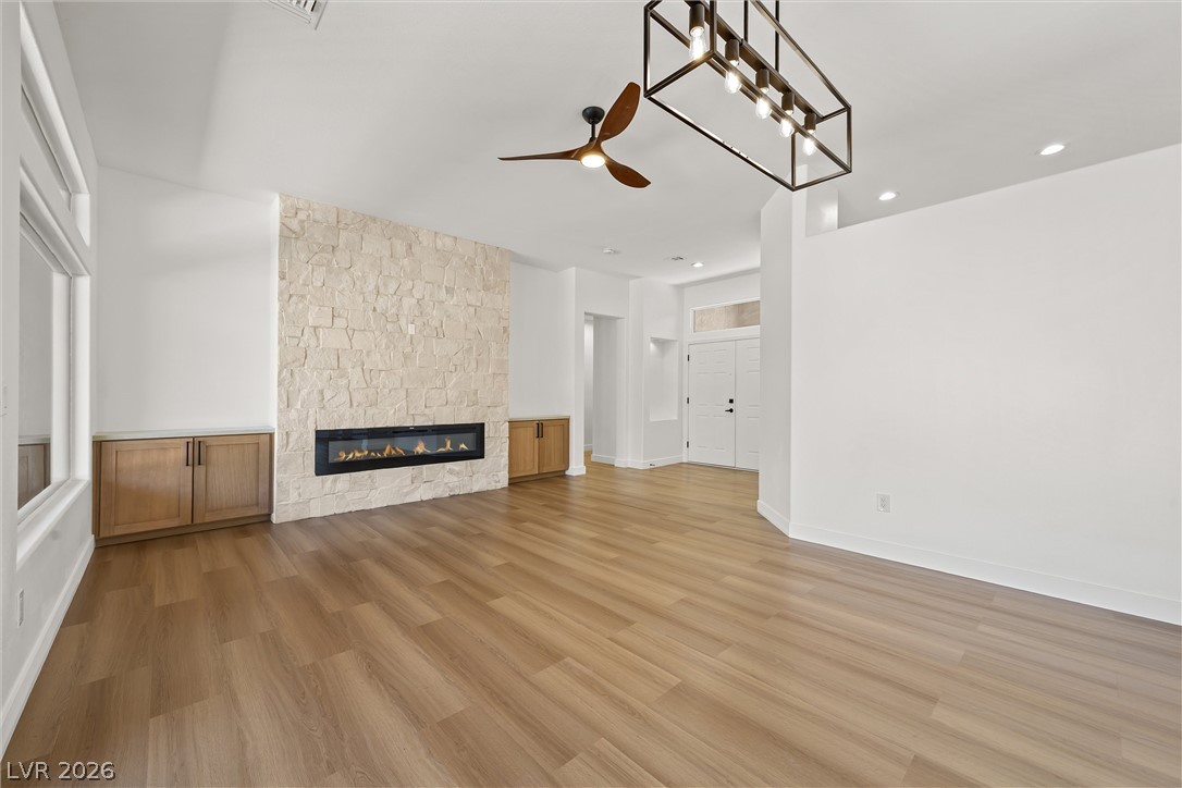 Unfurnished living room with a pale stone fireplace, built-in wood cabinets, and warm wood flooring.
