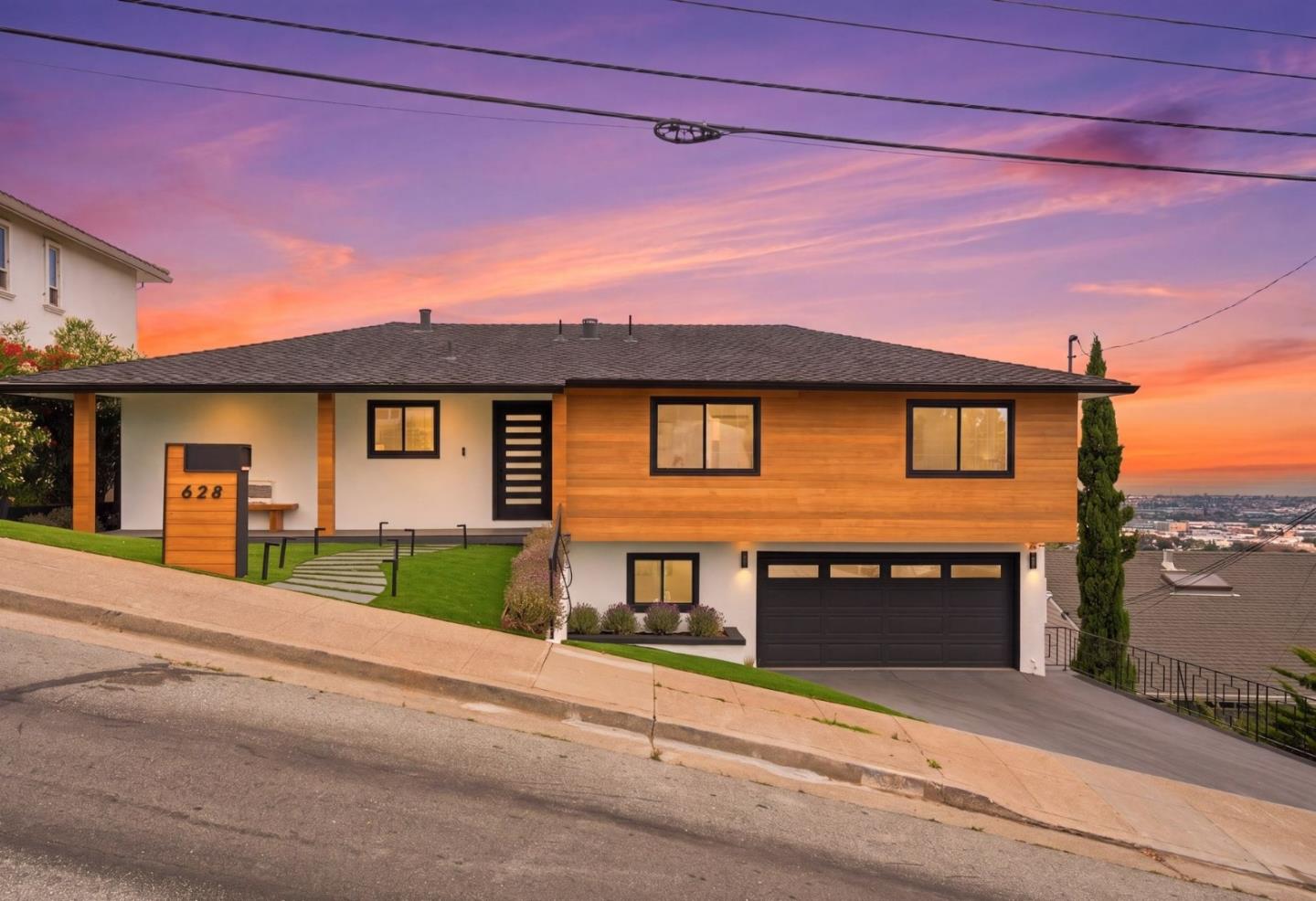 Modern split-level home with warm wood siding and black garage door at sunset.