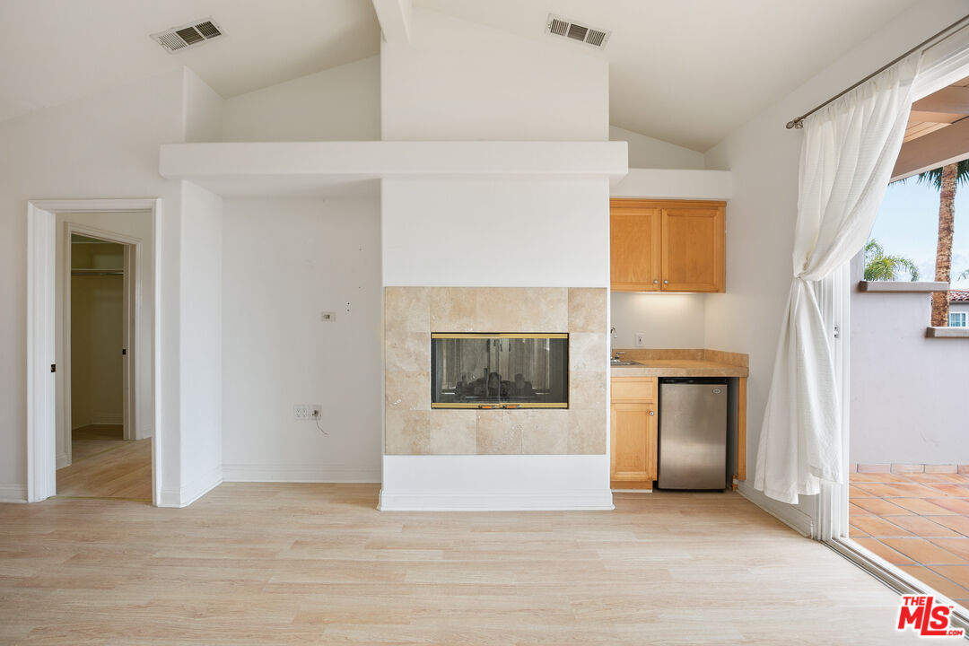 Vacant living area with a stone fireplace, kitchenette, and sliding doors to a tiled patio.