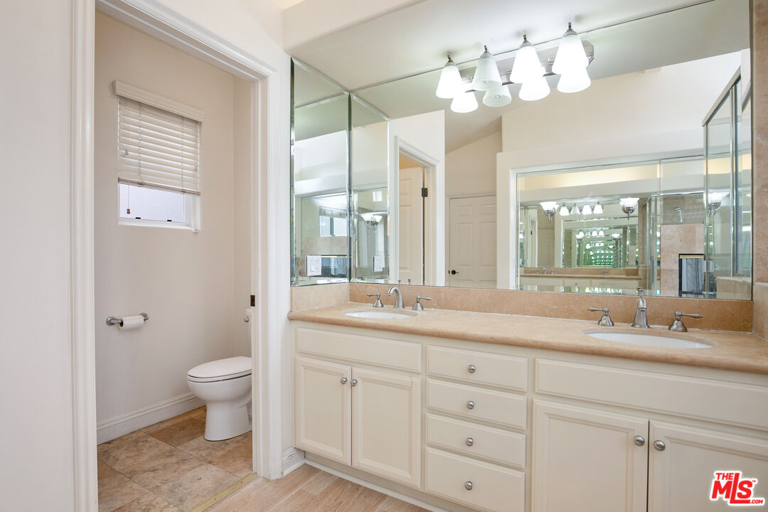 Bathroom with a double-sink vanity and mirrored wall beside a separate toilet room.