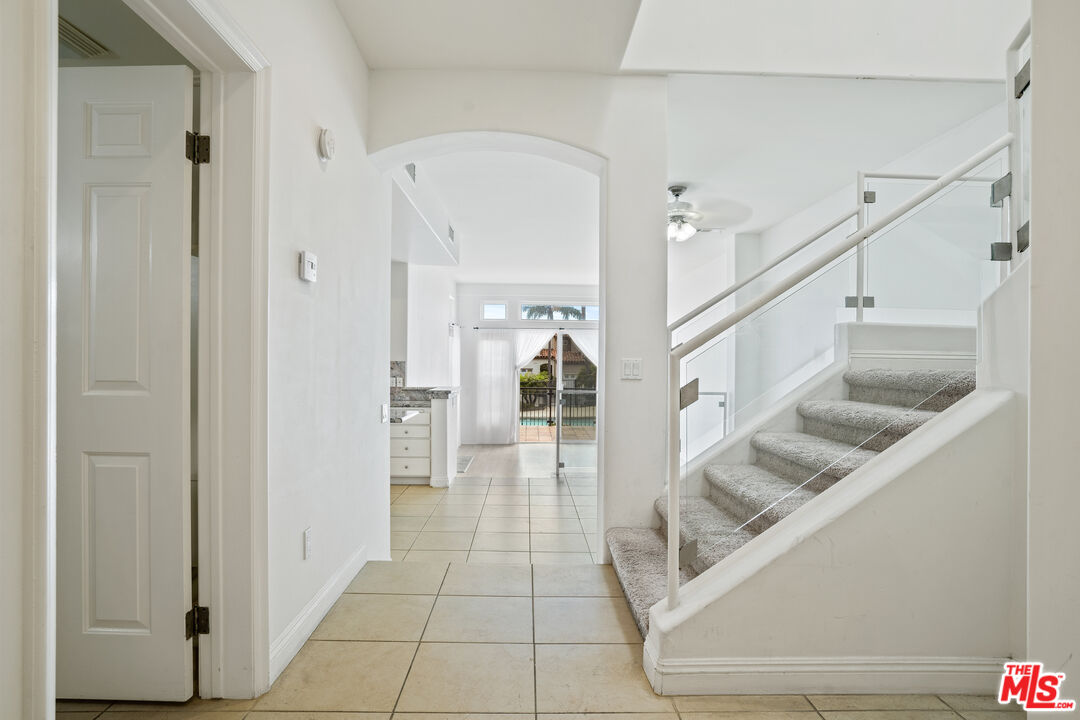 Entry hall with tiled floors, glass-railed carpeted stairs, and a view toward the kitchen and pool.
