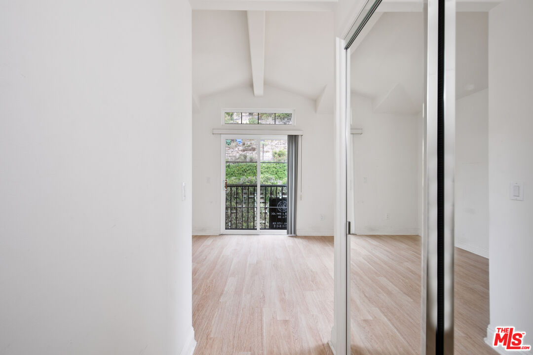 Vacant bedroom with mirrored closet doors, vaulted ceiling, and a sliding glass door to a balcony.