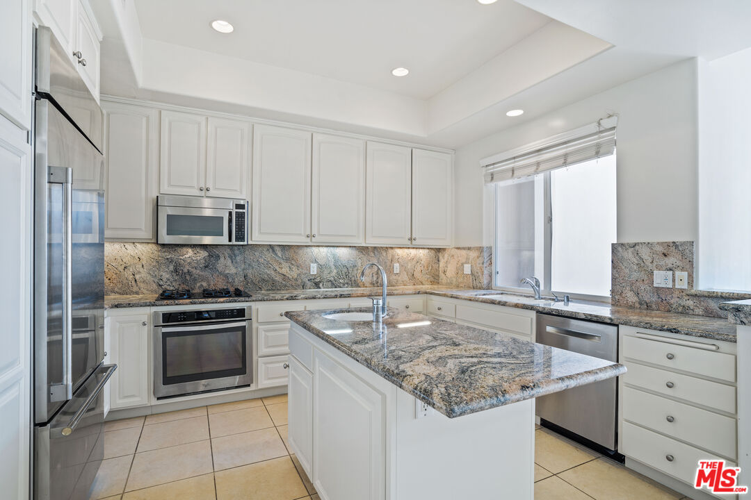 Bright kitchen with a granite-topped island, white cabinetry, and stainless steel appliances.